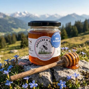 Bocal de miel de montagne Abeilles & Cîmes de Quentin Marion posé sur une pierre avec des fleurs bleues, un paysage de montagnes et de sapins en arrière-plan