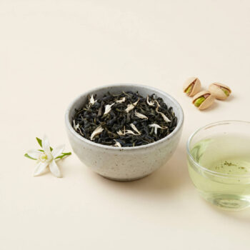 Bol de thé vert Dammann Frères avec des pistaches et une fleur d'oranger, évoquant les saveurs de pistache et de fleur d'oranger