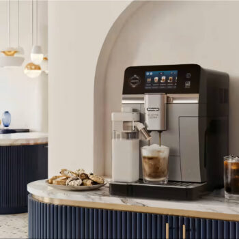 Machine à espresso De'Longhi Eletta Ultra préparant un café latte dans un verre, avec une carafe à lait à côté et des biscuits sur le comptoir