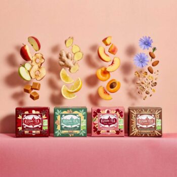 Quatre boîtes de Kusmi Tea alignées, avec des fruits et ingrédients flottants au-dessus : pomme, gingembre, pêche et amandes, symbolisant les infusions.