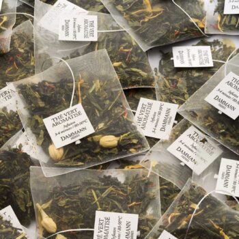 Vue rapprochée de nombreux sachets de thé vert aromatisé Dammann Frères, remplis de feuilles de thé et de morceaux de mangue, prêts à infuser