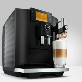 Machine à café automatique Jura E8 Piano Black préparant un latte macchiato dans un verre transparent, avec écran tactile affichant 'Mousse de lait'