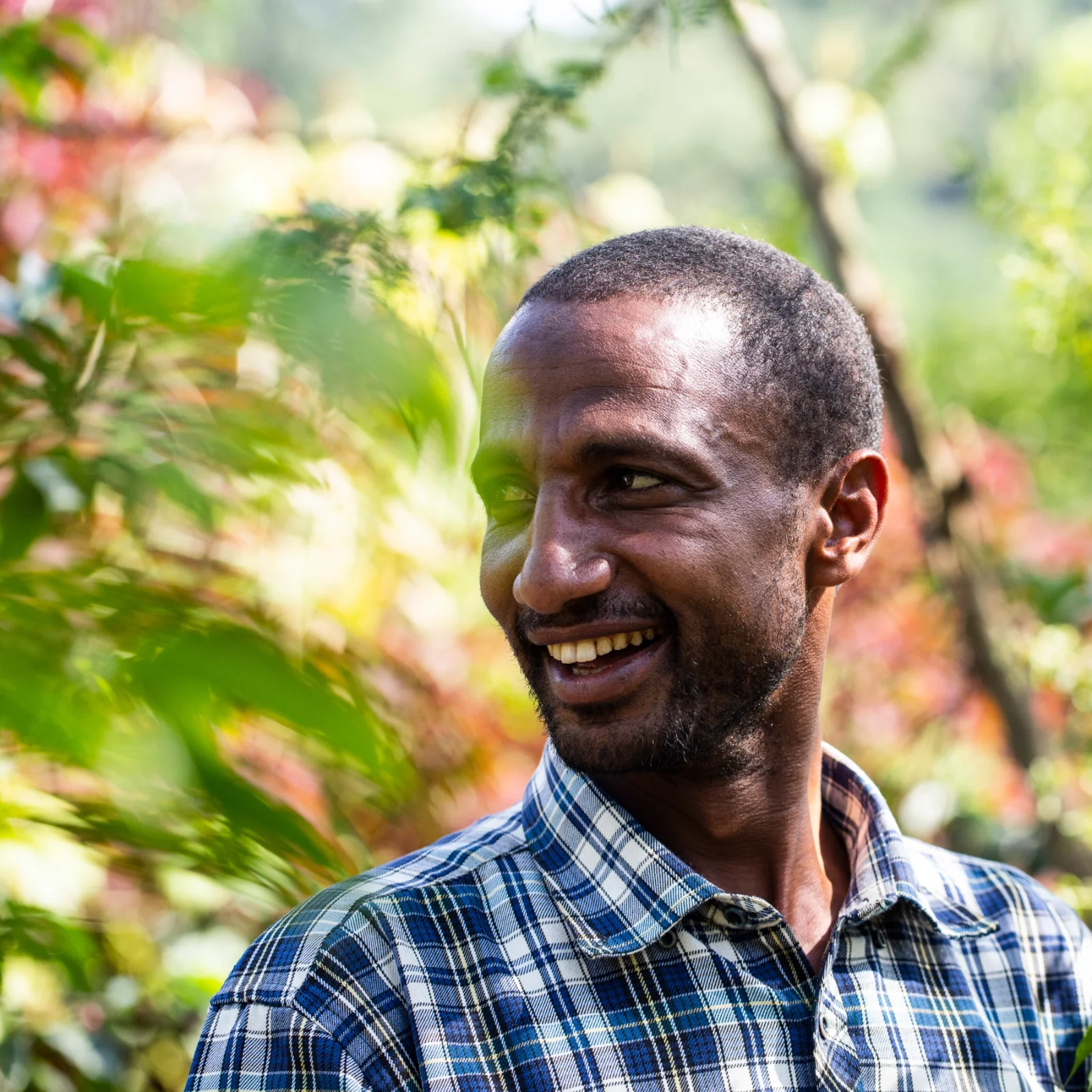 Khalid Shifa, producteur de café éthiopien, souriant dans un environnement verdoyant, portant une chemise à carreaux bleus et blancs