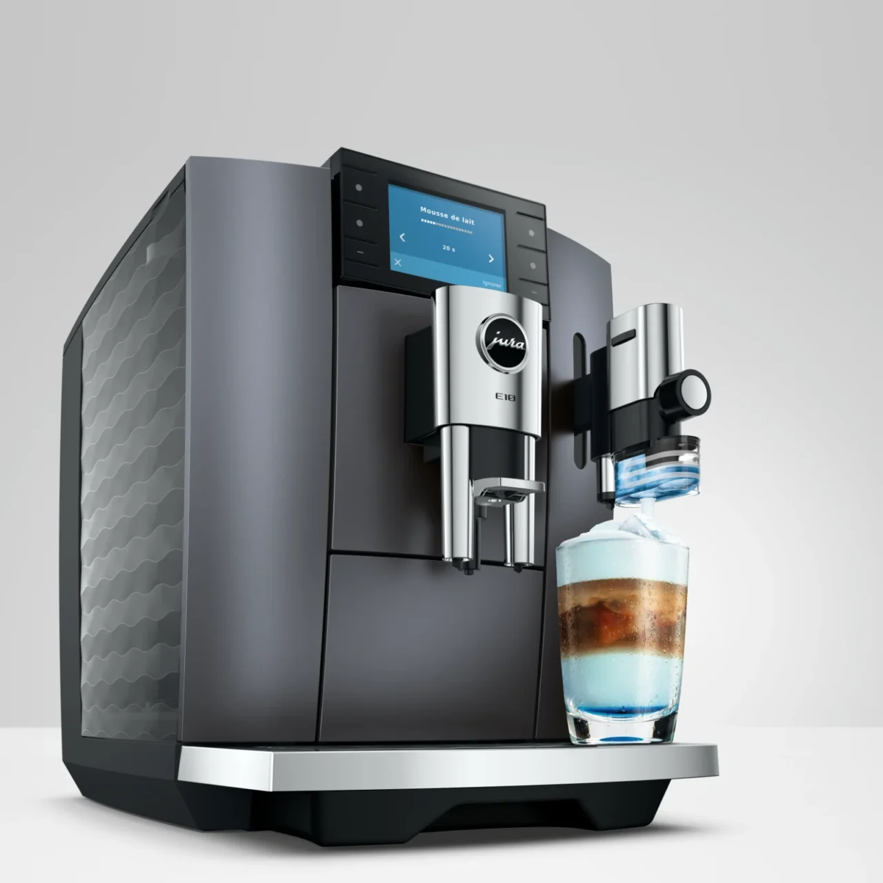 Machine à café automatique Jura E10 noire avec écran tactile, préparant une boisson lactée colorée dans un verre design sur le repose-tasse