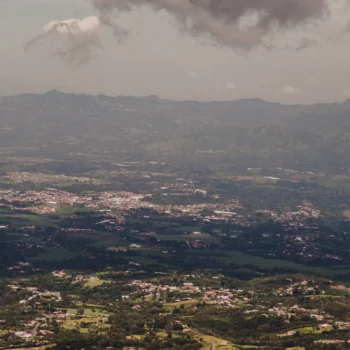 Vue panoramique en plongée sur des plantations de café et un village entouré de montagnes sous un ciel nuageux dans les terroirs