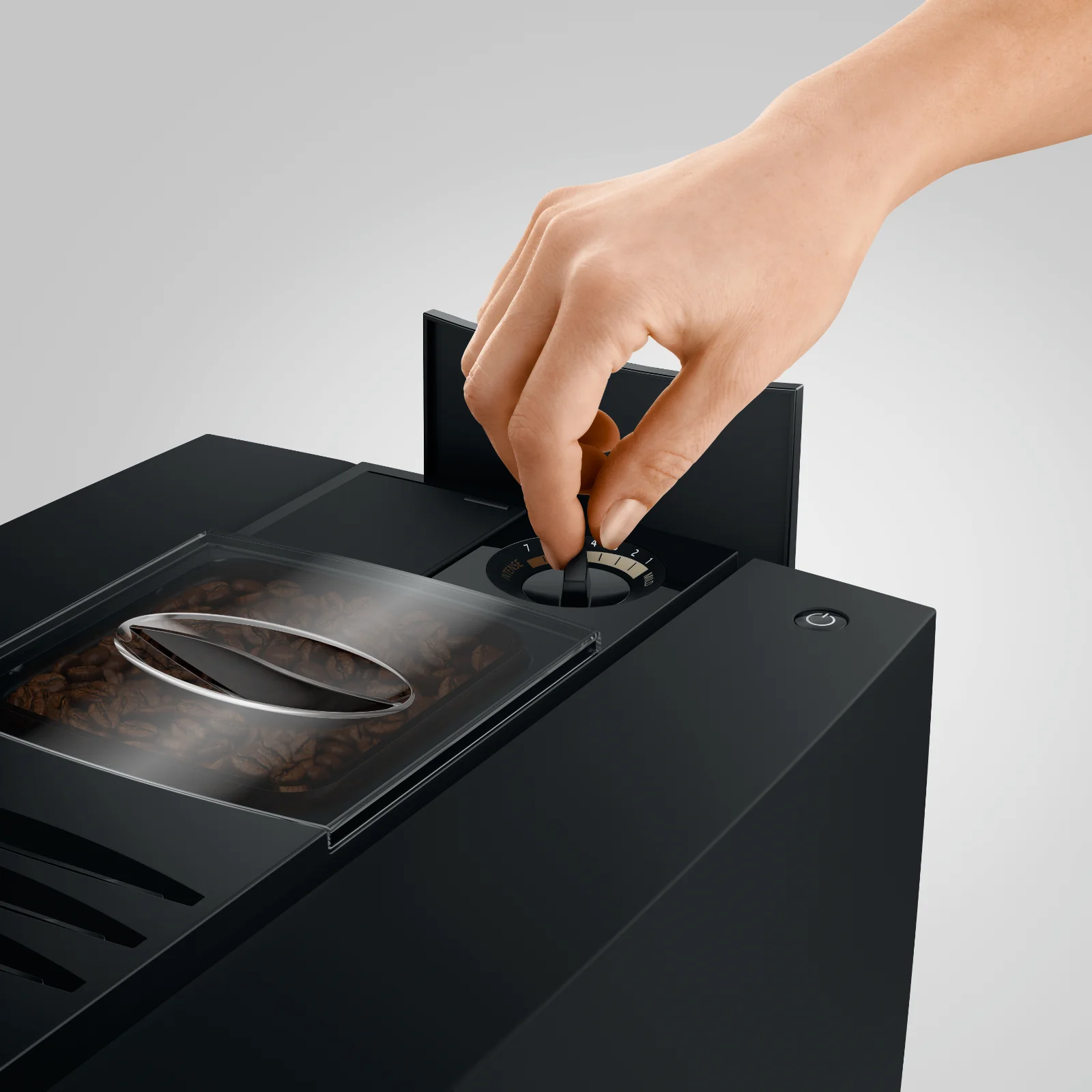 Main réglant la finesse de mouture sur le sélecteur d'une machine à café automatique, située à côté du bac à grains rempli