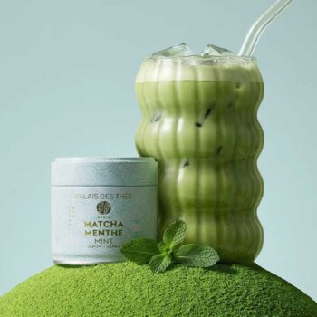 Boite de thé Matcha Menthe de Palais des Thes posée sur un tas de poudre de thé, accompagnée d'un verre ondulé rempli d'un matcha latte glacé.