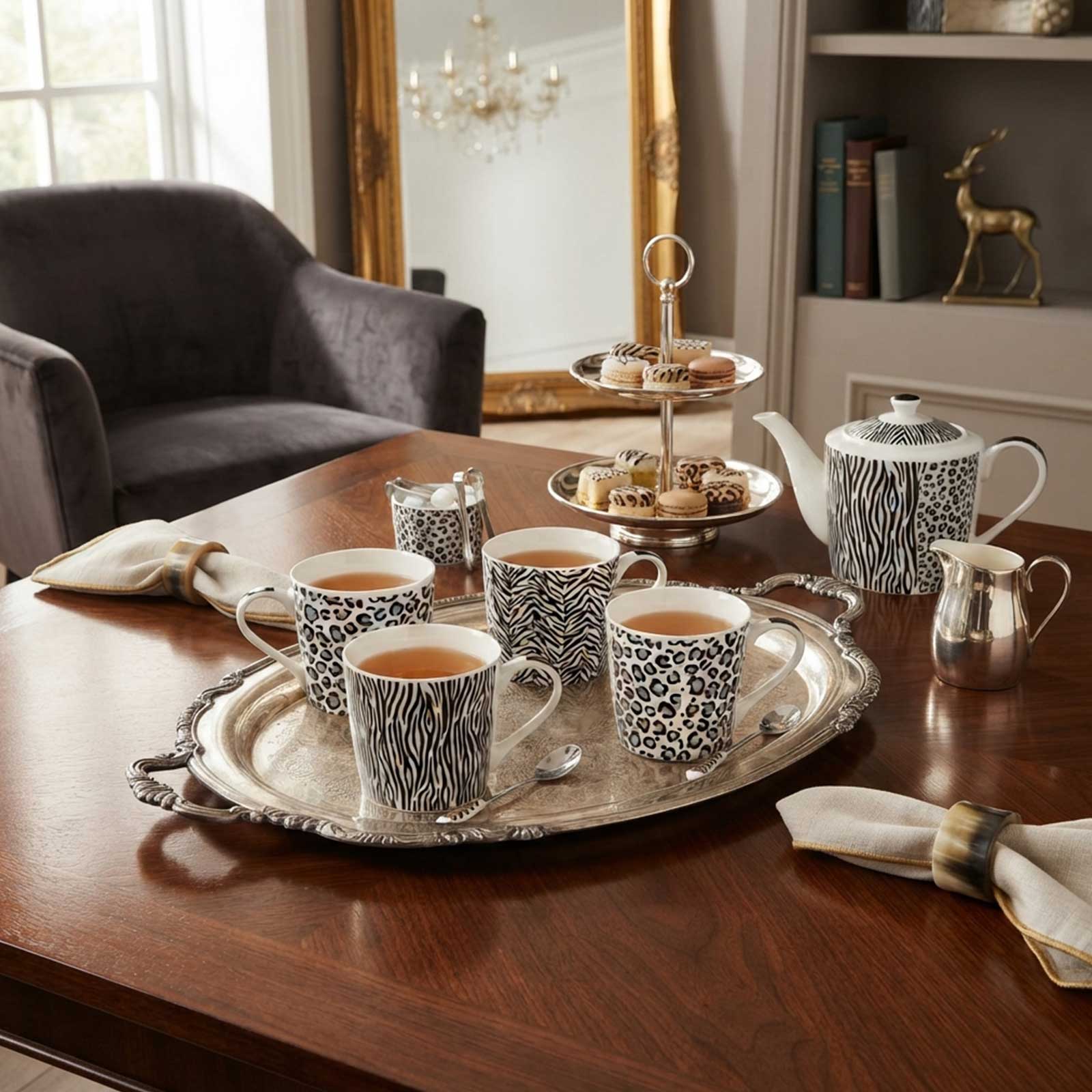 Service à thé en porcelaine avec motifs zèbre et léopard disposé sur un plateau en argent, incluant tasses, théière et présentoir à pâtisseries.