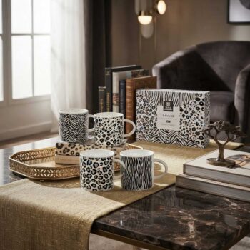 Quatre tasses Savane à motifs léopard et zèbre disposées sur des livres, accompagnées d'un coffret cadeau sur une table basse élégante