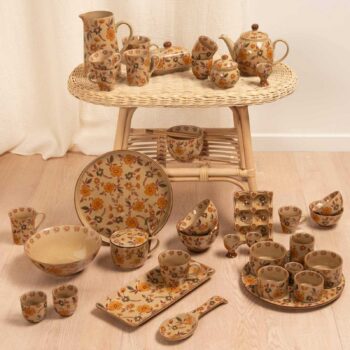 Service de vaisselle complet en céramique beige orné de motifs floraux orangés, disposé sur et sous une table basse en rotin