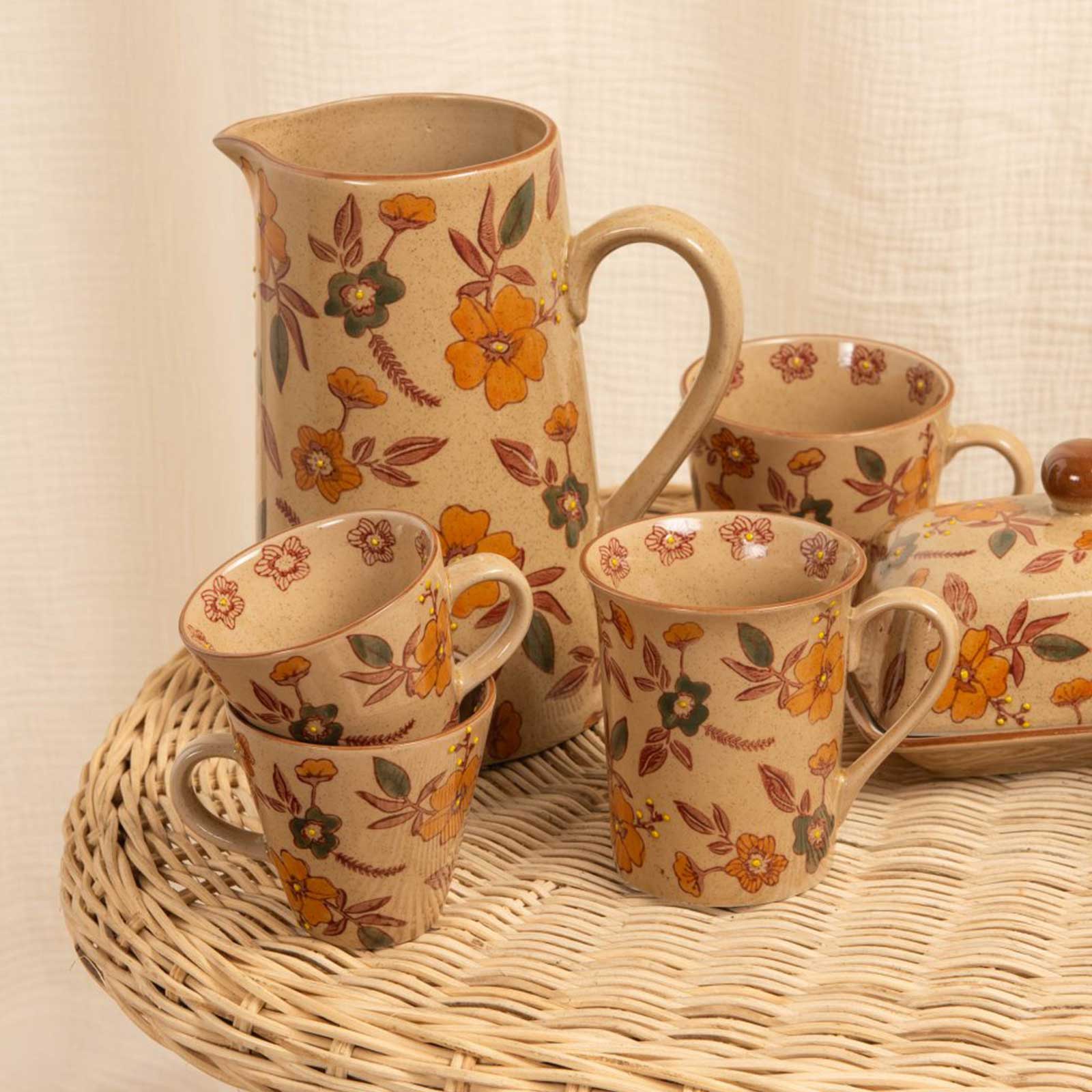 Service à thé en grès artisanal beige moucheté avec des motifs floraux orange, comprenant une théière, des tasses et un sucrier sur un plateau