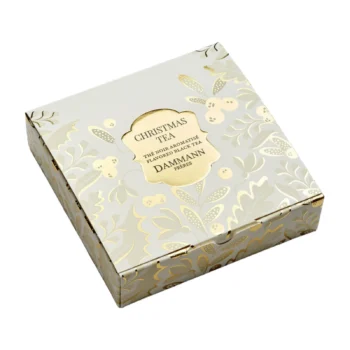 Boîte carrée de Christmas Tea Dammann Frères avec des motifs de feuilles et de baies dorées sur fond blanc cassé, présentée en vue en plongée