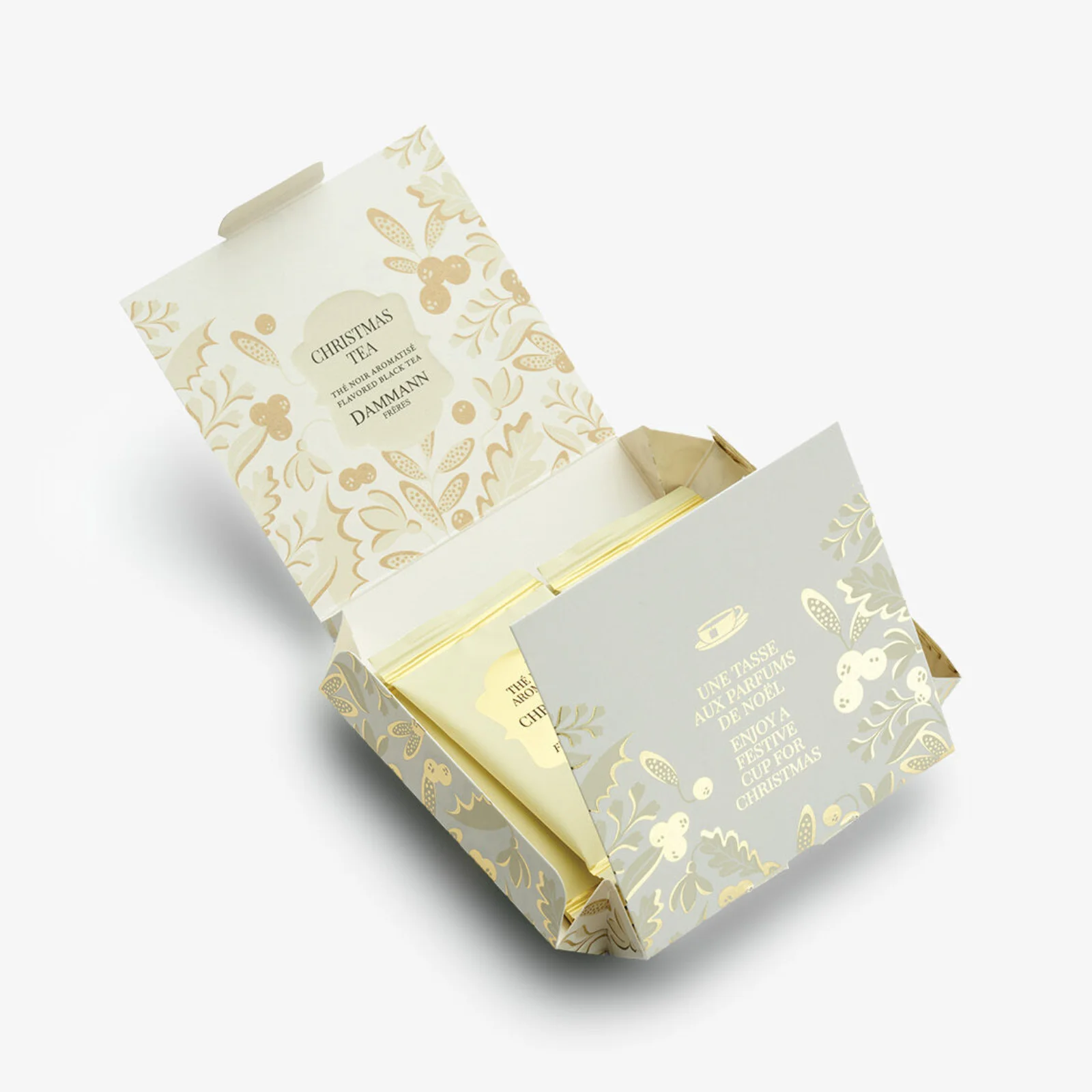 Boîte de thé noir aromatisé Dammann Frères pour Noël, ouverte, révélant des sachets de thé dans un emballage festif aux motifs végétaux dorés