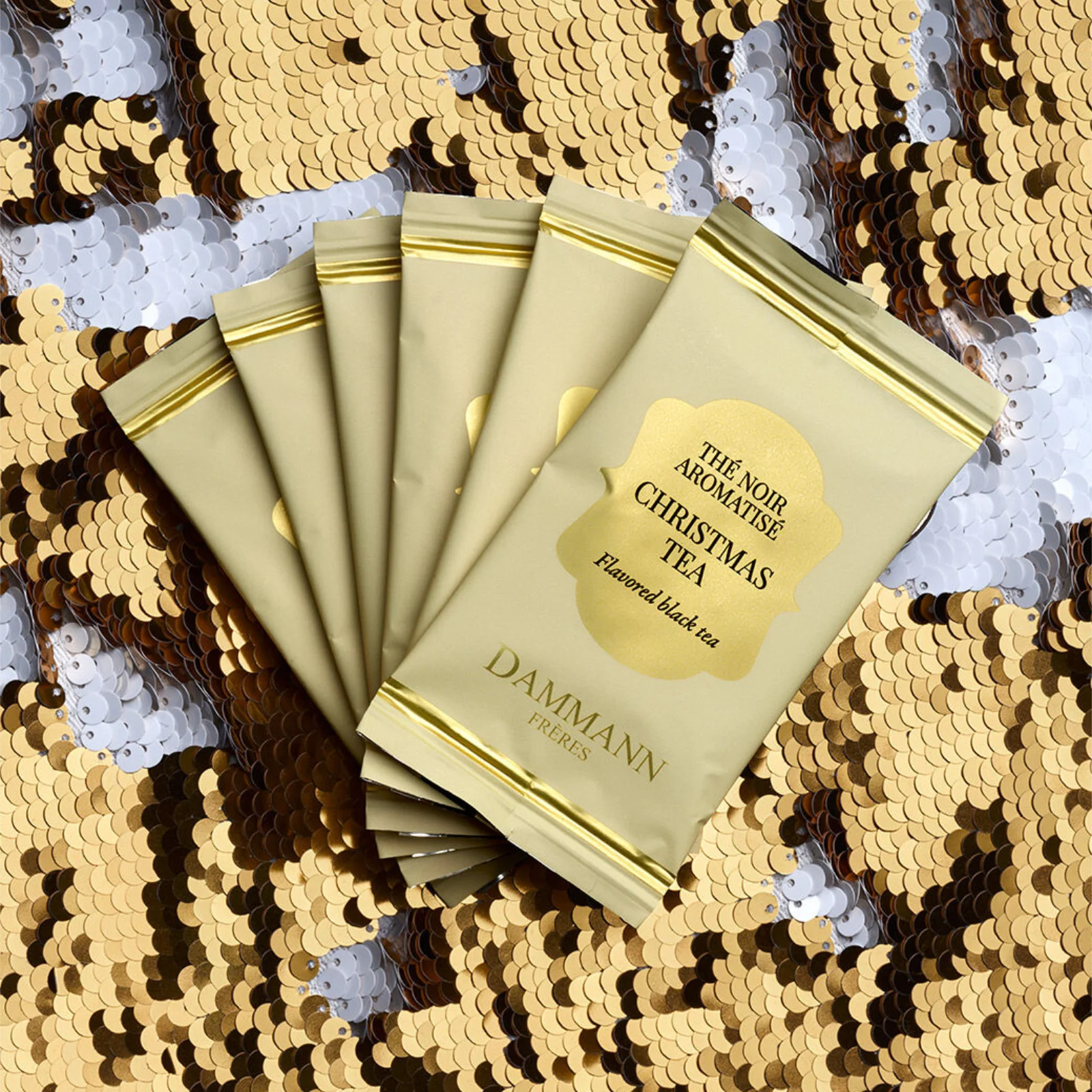 Sachets de thé noir parfumé Dammann Frères Christmas Tea disposés en éventail sur un fond de paillettes dorées et argentées