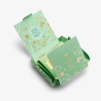 Coffret cadeau ouvert de Dammann Frères contenant des sachets de thé Infusion de Noël dans un emballage vert illustré de motifs végétaux dorés