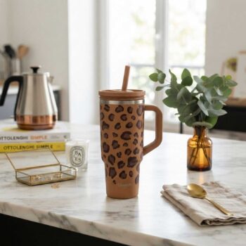 Gourde isotherme Qwetch avec motif léopard posée sur une table en marbre, accompagnée d'une paille et d'une anse intégrée