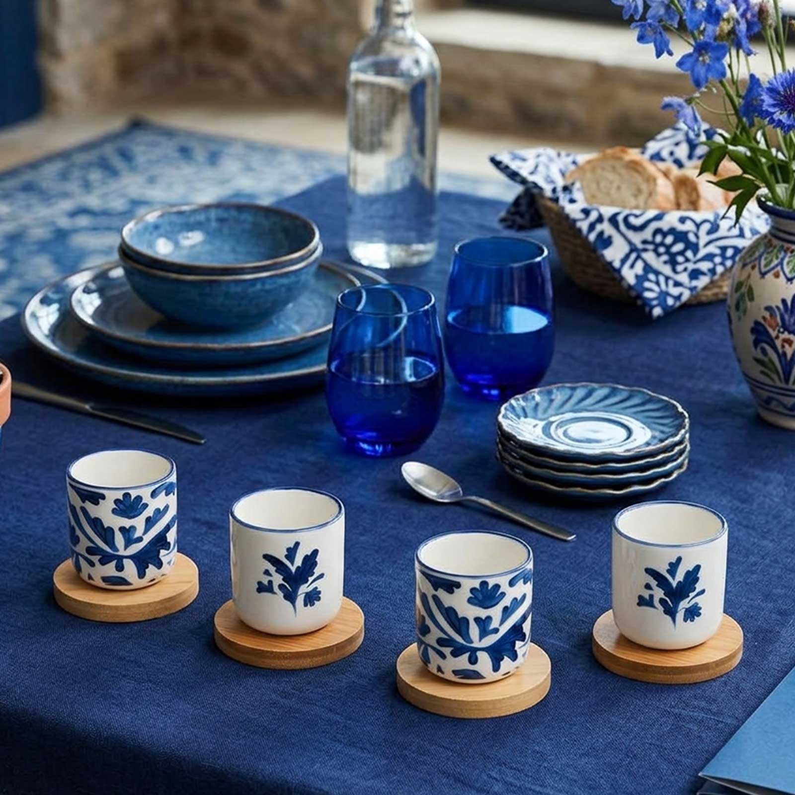 Quatre tasses en céramique peintes de motifs bleus floraux posées sur des sous-verres en bois sur une table dressée avec de la vaisselle bleue