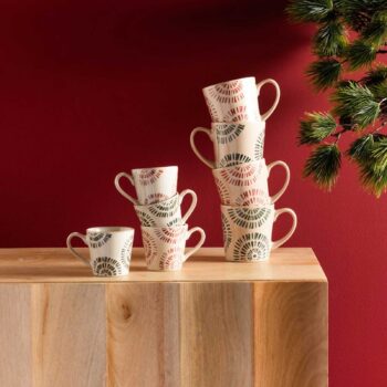 Ensemble de tasses en céramique à motifs graphiques circulaires, empilées et posées sur un buffet en bois clair devant un mur rouge bordeaux