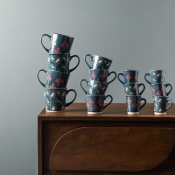 Piles de tasses en céramique bleu profond décorées de motifs floraux rouges et roses posées sur un buffet en bois sombre