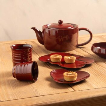 Service à thé en céramique rouge foncé composé d'une théière, de tasses et de tartelettes servies sur des coupelles en forme de pétales