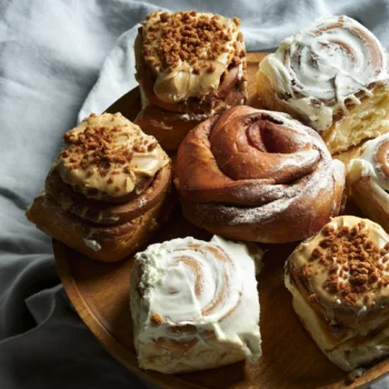 Assortiment de brioches à la cannelle sur un plateau en bois, certaines nappées de glaçage blanc, d'autres au caramel et éclats de spéculoos