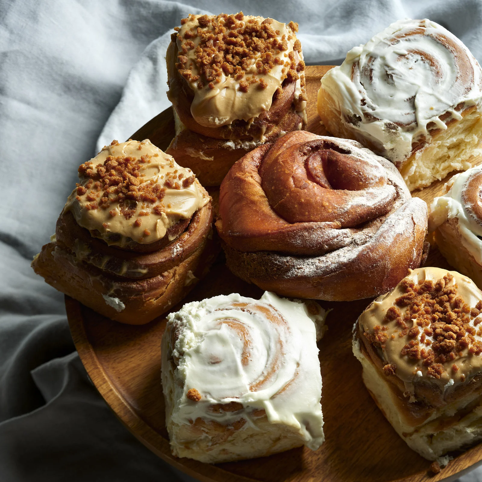 Assortiment de brioches à la cannelle sur un plateau en bois, certaines nappées de glaçage blanc, d'autres au caramel et éclats de spéculoos
