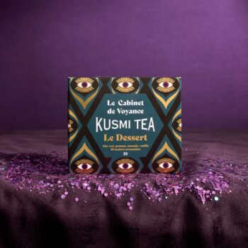 Boîte de thé Kusmi Tea Le Dessert entourée de paillettes violettes sur fond sombre, packaging bio aux motifs mystiques d'yeux