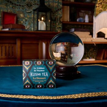 Boîte de thé Kusmi Tea Le Cabinet de Voyance posée sur une nappe en velours bleu à côté d'une boule de cristal dans un décor mystique