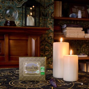 Boîte de thé noir Kusmi Tea Tsarevna posée sur une nappe sombre ornée de symboles, entourée de bougies allumées dans une ambiance mystique
