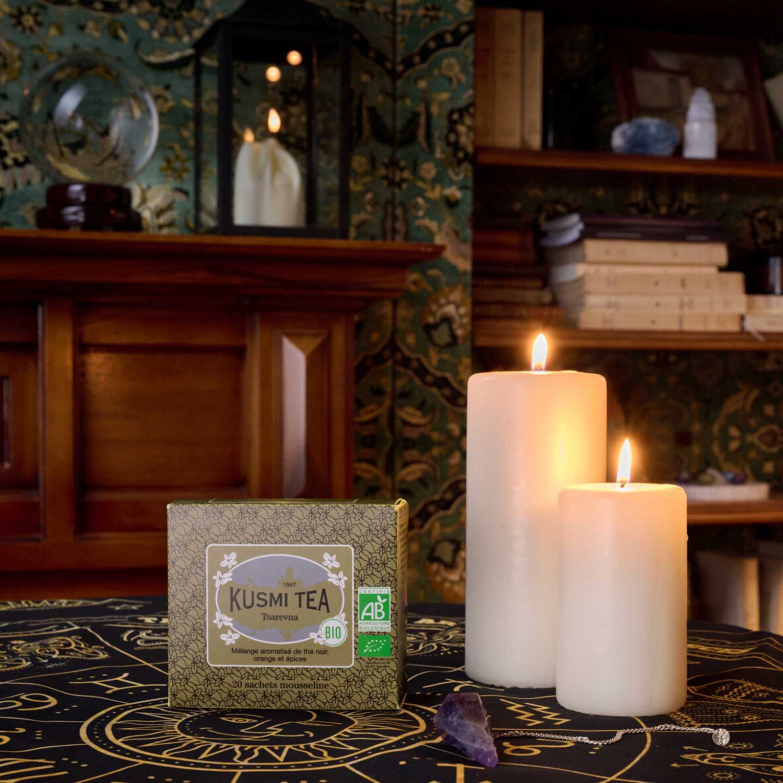 Boîte de thé noir Kusmi Tea Tsarevna posée sur une nappe sombre ornée de symboles, entourée de bougies allumées dans une ambiance mystique